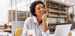 Mulher branca, com cabelo longo e &oacute;culos, sorrindo olhando para a tela do notebook.