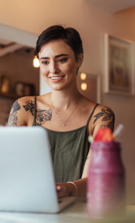 Mulher branca, com cabelo curto e tatuagens, mexendo no notebook.