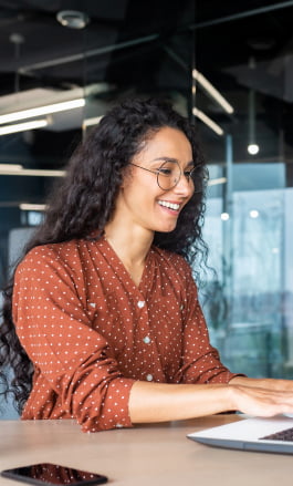 Mulher parda, com cabelo solto, usando &oacute;culos e mexendo no notebook.