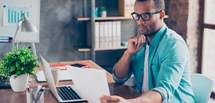 Homem negro, com cabelo curto e &oacute;culos, olhando para um papel.