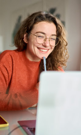 Mulher branca, com cabelo longo e &oacute;culos, sorrindo olhando para a tela do notebook.